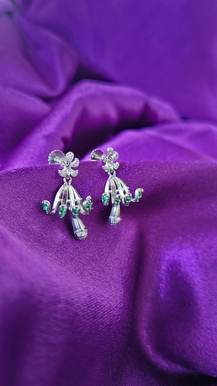 Pair of silver earrings with green gemstones on a purple fabric background